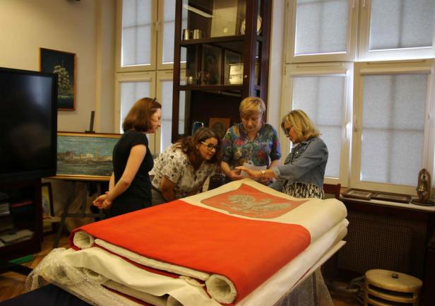 Przy galowej banderze; od lewej stoją: Anna Pawlak z Zespołu ds. Projekt&oacute;w - Dział Nauki UMG, Arleta Gałązka &ndash; kustosz &bdquo;Daru Pomorza&rdquo; (Narodowe Muzeum Morskie w Gdańsku), Joanna Stasiak &ndash; kustosz Sali Tradycji UMG i konserwator tkanin Mariola Ratajczyk